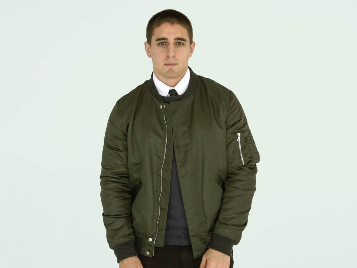 Seorang pria mengenakan jaket bomber berwarna hijau, dengan vest dan dasi